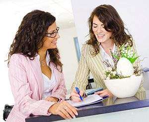 Happy businesswomen working together in team at office reception, looking at documents, talking, smiling.